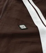 Campera deportiva de poliamida color marrón con detalles en blanco en los hombros y mangas. Presenta cierre frontal completo, cuello alto y puños elásticos.