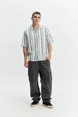 Camisa de manga corta oversize en tejido rústico, con diseño de rayas verticales celestes y blancas, cuello clásico y cierre frontal de botones.
