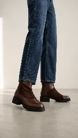 Bota corta de cuero color marrón, con diseño de texturas combinadas, talón con textura grabada, taco geométrico y cierre lateral.