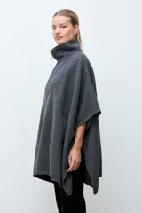Capa de paño gris con cierre frontal y cuello alto. Presenta un diseño con paneles superiores capitoneados en la zona del pecho y hombros, y aberturas laterales para los brazos.