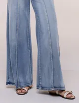 Jean wide leg de tiro alto en denim azul claro, con calce ajustado en la cadera, costuras verticales frontales y bolsillos estilo carpintero.