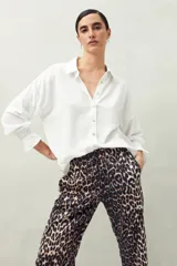 Camisa de manga larga color blanco con textura sutil, cuello clásico y cierre frontal de botones. Presenta un corte relajado y puños con frunces elásticos.