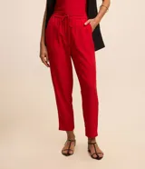 Pantalón de crepé rojo, modelo estilo pijama, de corte fluido, con cintura elástica y lazo de ajuste con terminales metálicas. Cuenta con bolsillos laterales y cierre frontal con cremallera y botón.