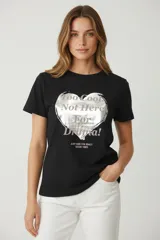 Remera negra de manga corta y cuello redondo, con estampado frontal de un corazón plateado con texto en rosa y plateado.