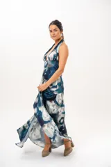Vestido largo con escote halter profundo y diseño sin mangas. Presenta un estampado difuminado en tonos azules, celestes, blancos y grises, con corte ajustado en el torso y una falda larga con vuelo.