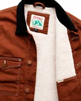 Campera estilo workwear de Denali, confeccionada en canvas resistente color marrón. Presenta interior forrado en corderito sherpa, cuello de pana negro, cierre frontal con botones metálicos color cobre y cuatro bolsillos frontales con costuras reforzadas en contraste.
