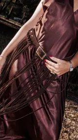 Cinturón artesanal de cuero color chocolate con hebilla cuadrada metálica y flecos largos que cuelgan a lo largo de la falda.