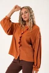 Camisa color naranja óxido con cuello mao, mangas largas abullonadas y cierre frontal con botones. Presenta un volante vertical con borde rojo en el frente.