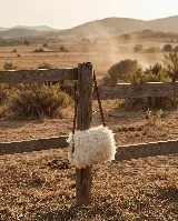 Cartera de cuero vacuno color beige con exterior de corderito sintético y correa de cuero marrón. Incluye forro y cierre.