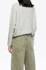 Sweater de punto color gris melange, confeccionado en una mezcla de lana y alpaca. Presenta un diseño de corte recto con escote redondo, mangas largas tipo murciélago con puños anchos y detalles de piedras brillantes aplicadas en toda la prenda.