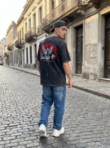 Remera negra con efecto lavado, corte oversize y estampado de palomas y texto en rojo.