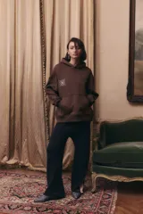 Buzo oversize de frisa color marrón chocolate, con capucha, bolsillo frontal tipo canguro y puños y ruedo acanalados. Presenta un estampado gráfico en el pecho.
