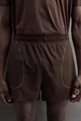 Short de running color marrón, confeccionado en tejido técnico elástico con forro interior. Cuenta con cintura elástica ajustable, bolsillos laterales con cierre de cremallera oculto y aberturas en las perneras.