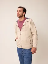 Campera de nylon color beige con cierre frontal, capucha ajustable y bolsillos laterales. Presenta un forro interno con diseño a cuadros.