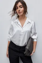 Camisa blanca de calce relajado con acabado satinado y brillo sutil, cuello clásico, cierre frontal con botones y mangas largas con puños.