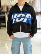 Campera tejida negra de algodón con corte boxy fit, cuello alto con cierre de doble carril y diseño gráfico en azul y blanco con letras en el pecho.