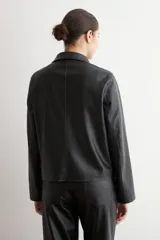Chaqueta de eco cuero negro con cuello camisero, cierre frontal oculto y mangas largas con puños rectos.