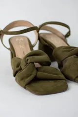 Sandalia de tacón cuadrado medio, confeccionada en material textil tipo gamuza color negro. Presenta un diseño de tiras cruzadas con nudo en la parte delantera y una tira ajustable con hebilla metálica en el tobillo.