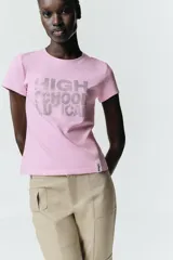 Camiseta de algodón con efecto lavado, color rosado, de corte regular, cuello redondo y manga corta. Presenta un estampado frontal con el texto High School Musical realizado en strass brillante.