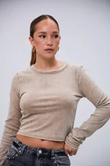 Remera beige de manga larga con efecto acid wash y cuello redondo decorado con tachas plateadas.