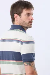 Remera polo de manga corta con cuello y puños en azul oscuro. Presenta un diseño de rayas horizontales en tonos de azul claro, azul oscuro, blanco, amarillo, rosa y verde. Incluye botones personalizados y un logo bordado en el pecho.