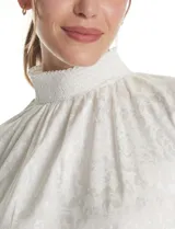 Blusa de gasa labrada color blanco, con cuello alto en punto smock, mangas largas con terminación fruncida y diseño elegante.