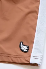 Short de baño color ladrillo con cintura elástica y cordón ajustable. Presenta una franja lateral blanca estilo esmoquin, dos bolsillos laterales y uno trasero con cierre.