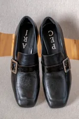 Mocasín de cuero vacuno color azul, con punta cuadrada, taco bloque bajo y detalle de tira con hebilla metálica plateada en el empeine.