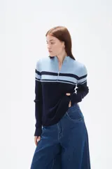 Polera de punto acanalado con diseño de bloques de color en azul claro y azul marino. Presenta cuello alto con cierre frontal y mangas largas.