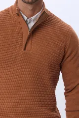 Buzo de punto color beige, con cuello alto y cierre frontal con cremallera y solapa de gamuza con botón. Presenta un tejido texturizado en el cuerpo y mangas lisas.