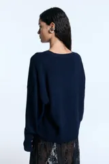Sweater de tejido de punto color azul marino, con diseño de silueta holgada, cuello redondo y mangas largas con puños acanalados anchos que incluyen orificio para el pulgar. Presenta un detalle de aplicación de hotfix brillante en el frente.