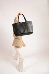 Cartera tipo tote de cuero graneado negro, con diseño clásico y textura uniforme. Cuenta con doble asa de hombro, bolsillo frontal con cierre magnético, bolsillo trasero con cierre metálico y compartimento principal con cierre. El interior está forrado y dispone de múltiples bolsillos organizadores.