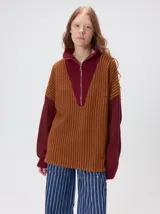 Pullover de tejido acanalado grueso con diseño bicolor en tonos marrón y bordó. Presenta cuello alto con cierre frontal, mangas largas y corte holgado.