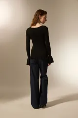 Remera de punto al cuerpo con cuello bote y mangas largas terminadas en volados acampanados. Presenta un ruedo con detalle de volados.