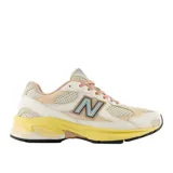 Championes urbanos New Balance modelo 2010, con diseño en tonos beige, crema y amarillo. Presenta una combinación de malla y gamuza en el exterior, con el logo N característico en el lateral y una suela de goma con entresuela amarilla destacada.