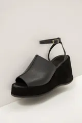Sandalia de plataforma corrida de cuero marrón, con capellada ancha y tira fina ajustable al tobillo con hebilla metálica.