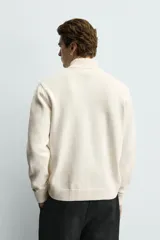 Chaqueta regular fit de punto color beige con cuello perkins, manga larga y cierre frontal con cremallera.
