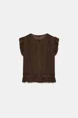 Blusa de cuello redondo y manga sisa con volantes, color marrón, con detalles de entredoses a tono, jaretas delanteras y cierre frontal con botones.