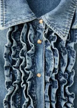 Camisa de denim estilo vaquero, con cuello camisero, manga larga con puños abotonados, cierre frontal con botones y detalle de volantes en el frente.