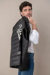 Chaleco de cuero negro con cierre frontal y cuello mao. Diseño acolchado horizontal.