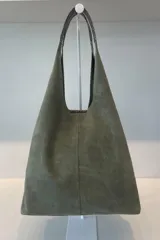 Bolso tipo tote de gran capacidad, confeccionado artesanalmente en cuero vacuno color marrón. Presenta un diseño minimalista con costura central vertical, fuelle lateral ajustable con cierre y placa metálica con logo en la parte inferior.