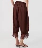 Pantalón bloomer marrón de cintura alta, confeccionado en viscosa con textura crinkle. Cuenta con un diseño amplio y cómodo, perneras voluminosas, puños con elástico interno y aplicación de encaje floral en los puños.