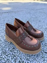 Mocasines de cuero negro con plataforma y suela de goma, decorados con tachas metálicas plateadas en el empeine y el talón.