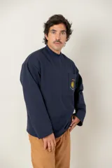 Buzo de cuello redondo color azul marino, con manga larga y corte holgado. Presenta un bolsillo frontal en el pecho con un bordado del sol de la bandera uruguaya, cuatro estrellas y la frase 'Heroicos sabremos cumplir'.
