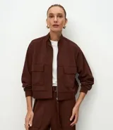 Campera de corte recto y largo, color marrón chocolate, con cuello alto, cierre frontal completo y bolsillos frontales tipo cargo con solapa. Presenta puños y ruedo acanalados.