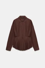 Camisa de cuello solapa y manga larga, confeccionada en popelín. Presenta un diseño con cintura entallada mediante pliegues y cierre frontal con botones ocultos por solapa.