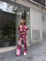 Conjunto de dos piezas compuesto por un buzo corto de manga larga y un pantalón de pierna ancha, confeccionado en tela morley elastizada con estampado tie-dye en tonos fucsia y marrón.
