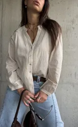 Camisa de manga larga color beige con diseño abotonado frontal, cuello mao y detalles de bordados y encaje en el frente y las mangas.