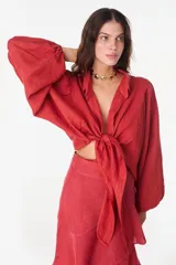 Top blanco de manga larga con diseño abullonado, cuello camisero y cierre frontal de botones, con detalle de nudo ajustable en la parte inferior y textura floral sutil en relieve.