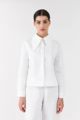 Camisa blanca de lino con mangas largas, cuello camisero grande en punta y cierre frontal con botones.